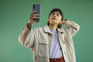 Junge Frau nimmt Selfie durch Handy gegen grünen Hintergrund - AXHF00294