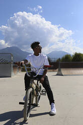 Young man sitting on BMX bike at skatepark - SYEF00222