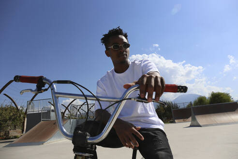 Mann mit Sonnenbrille sitzt auf BMX-Rad im Skatepark - SYEF00223
