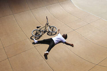 Young man lying down by BMX bike at skatepark - SYEF00227