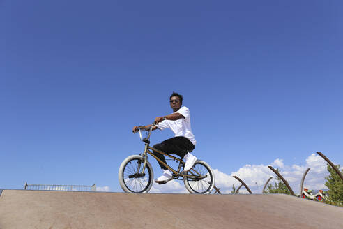 Mann sitzt auf BMX-Rad unter Himmel an sonnigem Tag - SYEF00229