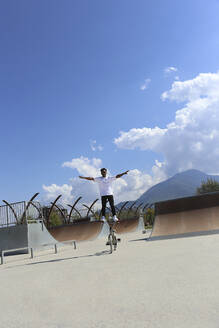 Mann auf BMX-Rad stehend mit ausgestreckten Armen im Skatepark - SYEF00230