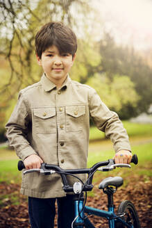 Smiling boy with bicycle standing at park - PWF00768