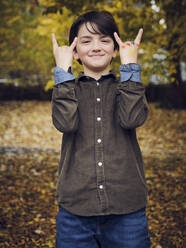 Lächelnder Junge mit Hupenzeichen im Park stehend - PWF00779