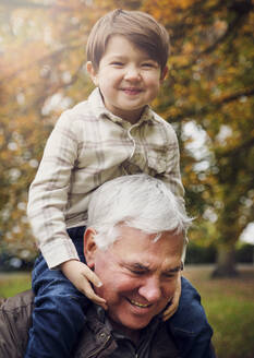 Smiling boy sitting on grandfather's shoulder at park - PWF00781