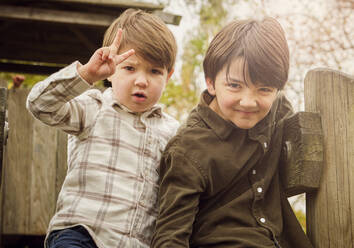 Boy making peace sign by brother playing at park - PWF00786