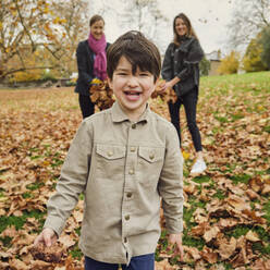 Happy boy standing on autumn leaves at park - PWF00794