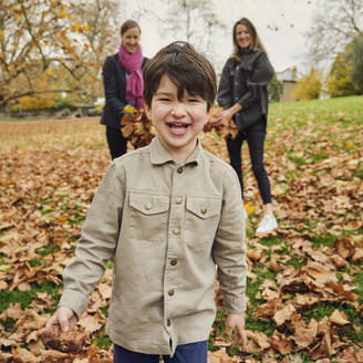 Glücklicher Junge auf Herbstblättern im Park stehend - PWF00794