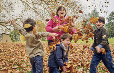 Großmutter spielt mit Enkelkindern, die im Park Herbstblätter werfen - PWF00795