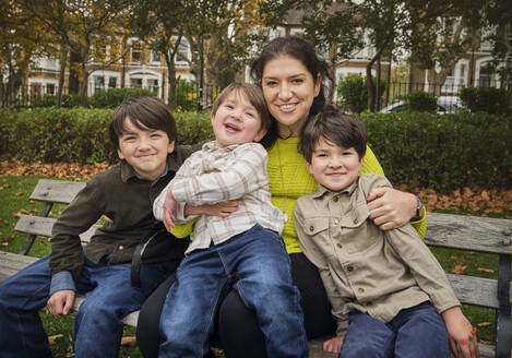 Lächelnde Frau sitzt mit Jungen auf einer Bank im Park - PWF00802