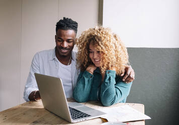 Happy business people sitting with laptop at desk in office - AMWF01152