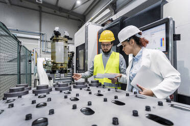 Ingenieur mit Kollege bei der Analyse von Maschinenteilen in der Fabrik - AAZF00105