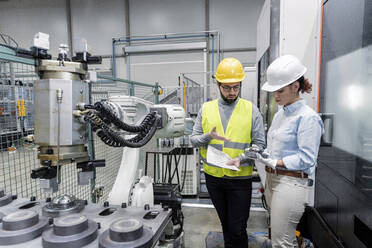 Junger Ingenieur erklärt einem Kollegen ein Maschinenteil in einer Fabrik - AAZF00115