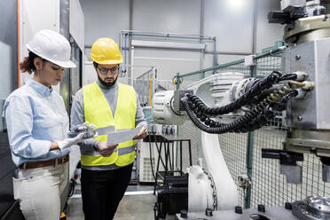 Engineer and colleague discussing over machine part in factory - AAZF00116