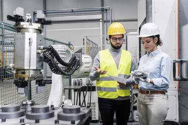 Businesswoman showing machine part to engineer in factory - AAZF00118