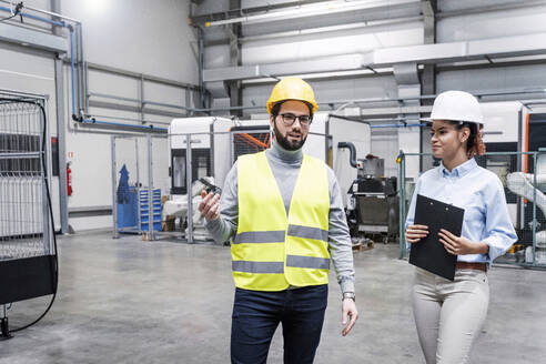 Lächelnder Ingenieur im Gespräch mit einem Kollegen in einer Fabrik - AAZF00126