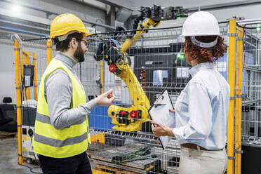 Engineers examining robotic arm in factory - AAZF00127