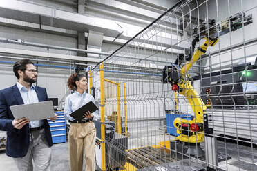 Business colleagues examining robotic arm in factory - AAZF00128