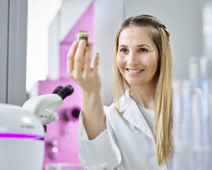 Glückliche Wissenschaftlerin mit blondem Haar, die im Labor Pflanzen analysiert - CVF02331