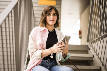 Frau mit Smartphone auf einer Treppe sitzend - JJF00274