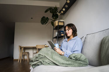 Woman using tablet PC sitting on sofa at home - JJF00290