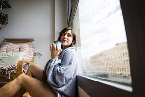 Nachdenkliche Frau mit Kaffeetasse am Fenster sitzend, zu Hause - JJF00292