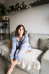 Nachdenkliche Frau sitzt zu Hause auf dem Sofa - JJF00294