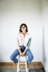 Woman wearing eyeglasses sitting on stool at home - JJF00301