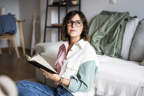 Nachdenkliche Frau sitzt mit Buch zu Hause - JJF00302