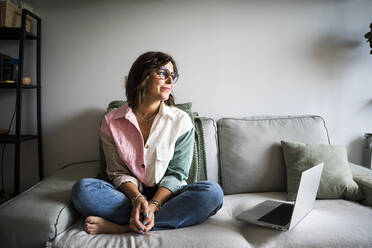 Contemplative woman with laptop sitting on sofa - JJF00310