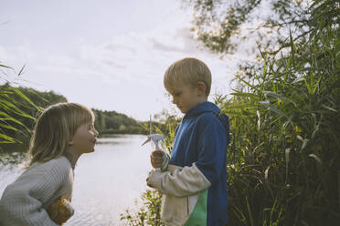 Junge und Mädchen spielen mit einem Windradmodell am See - NDEF00362