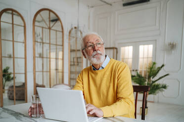 Thoughtful senior freelancer with laptop sitting at desk - MDOF00656