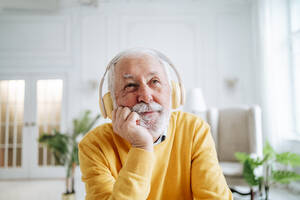 Thoughtful senior man listening to music through headphones at home - MDOF00660