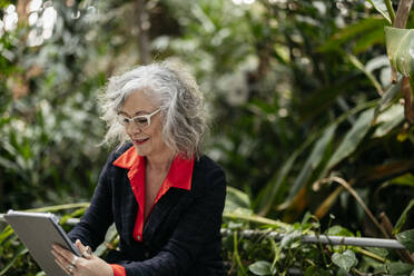 Businesswoman using tablet PC in garden - JCCMF09501