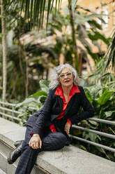 Ältere Geschäftsfrau sitzt auf einem Stuhl im Garten - JCCMF09507
