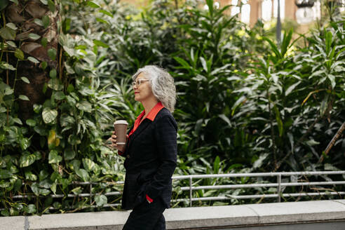 Geschäftsfrau mit Einwegbecher beim Spaziergang im Garten - JCCMF09510