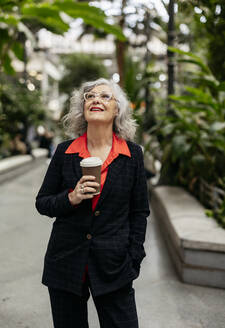 Kontemplative reife Geschäftsfrau mit Einweg-Kaffeebecher im Garten stehend - JCCMF09513