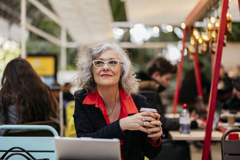 Nachdenkliche Geschäftsfrau mit Einweg-Kaffeebecher im Café sitzend - JCCMF09517