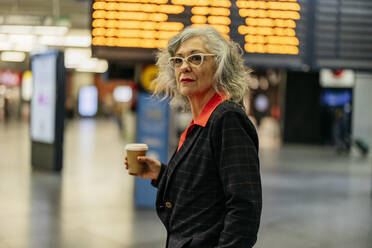 Mature businesswoman with disposable coffee cup standing at station - JCCMF09522