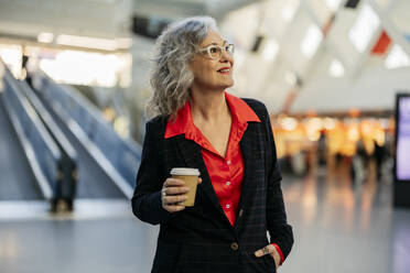 Happy mature businesswoman with disposable coffee cup at subway station - JCCMF09525