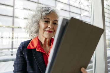 Lächelnde reife Geschäftsfrau mit grauem Haar, die einen Tablet-PC benutzt - JCCMF09538