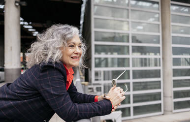 Thoughtful smiling businesswoman with gray hair leaning on railing - JCCMF09559