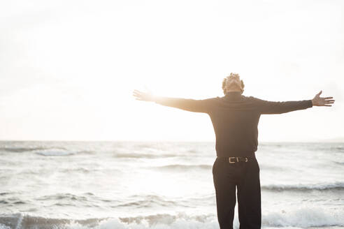 Carefree man with arms outstretched standing in front of sea - JOSEF17248