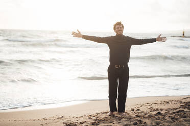 Carefree man with arms outstretched standing at beach - JOSEF17251