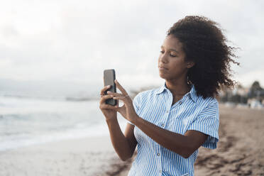 Junge Frau fotografiert mit ihrem Smartphone am Strand - JOSEF17252