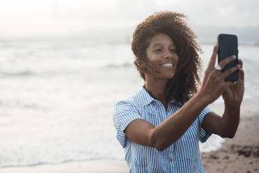 Glückliche junge Frau nimmt Selfie durch Smartphone am Strand - JOSEF17254