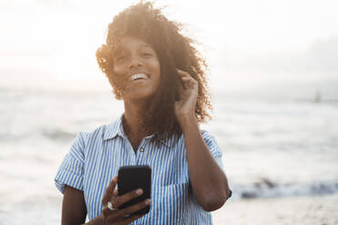 Glückliche Frau mit Smartphone vor dem Meer bei Sonnenuntergang - JOSEF17256