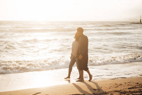 Man and woman walking on beach coastline at sunset - JOSEF17272