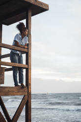 Nachdenkliche junge Frau, die bei Sonnenuntergang auf der Rettungsschwimmer-Hütte steht - JOSEF17274