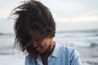 Smiling woman with curly hair at beach - JOSEF17279